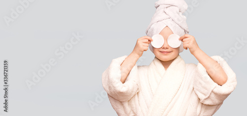 Banner view of beautiful kid girl with towel on head hold cotton pad disk cleansing face skin with cleanser. Happy girl remove makeup enjoy healthy clean skincare beauty treatment concept