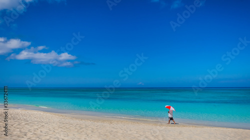 Fototapeta Naklejka Na Ścianę i Meble -  Man with a Umbrella walking on the deserted Seven Mile Beach in the Caribbean during confinement, Grand Cayman, Cayman Islands