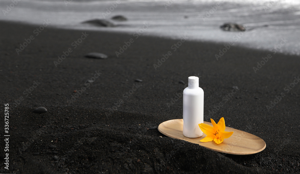 Clear white cosmetics tube on bamboo plate. Skincare tube product on black canarian sand with stones and ocean waves with white foam at the blurred background. Clear white cosmetics tube on bamboo plate. Skincare tube product on black canarian sand with stones and ocean waves with white foam at the blurred background.