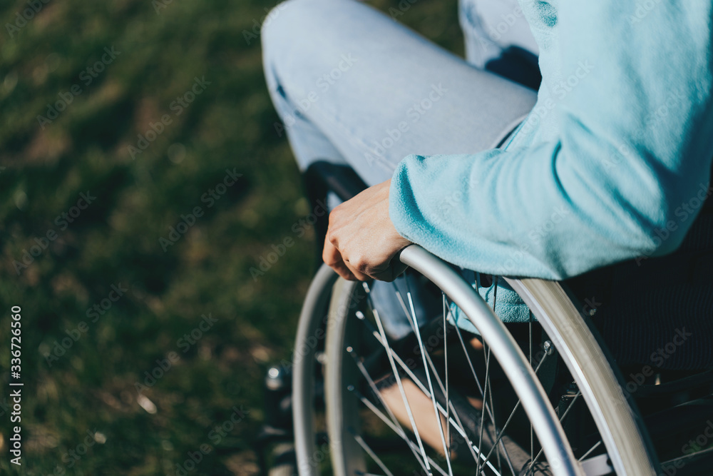 Obraz premium Close up of a young woman in a wheelchair while walking in a park on a sunny day. Recovery and healthcare concepts.