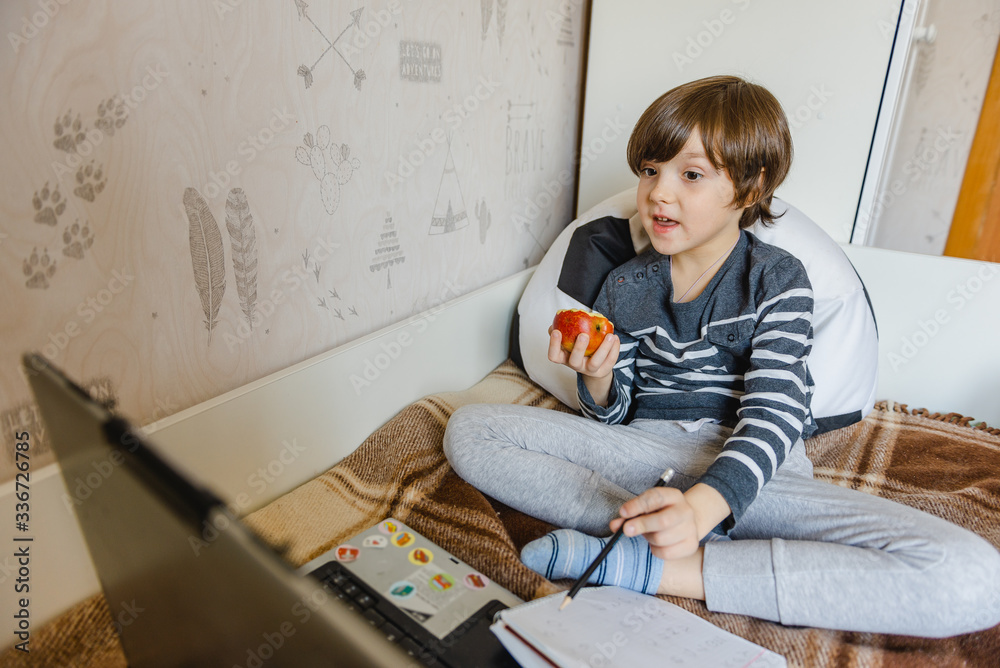 Distance learning for children during the coronavirus epidemic. The boy sits on the bed and receives a school assignment using the Internet and a laptop. Distance learning for children during the coronavirus epidemic. The boy sits on the bed and receives a school assignment using the Internet and a laptop.