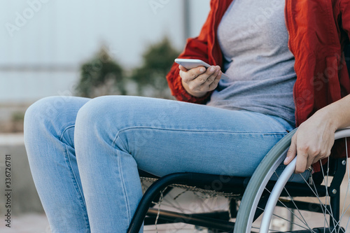A woman in a wheelchair with a phone in her hand walks on the street, her hand is close up, an unrecognizable man.