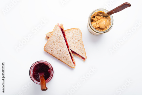 Peanut butter and jelly sandwich halves and glass jars on a white background, top view