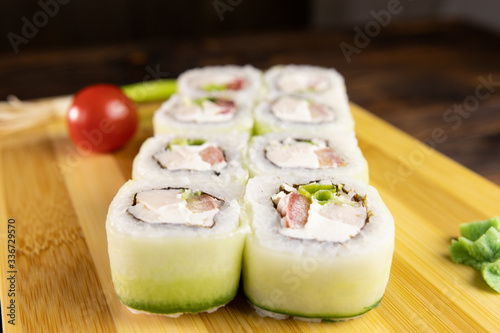 sushi rolls with cucumber, chicken, green leek and tomato on wooden board with wasabi side view
