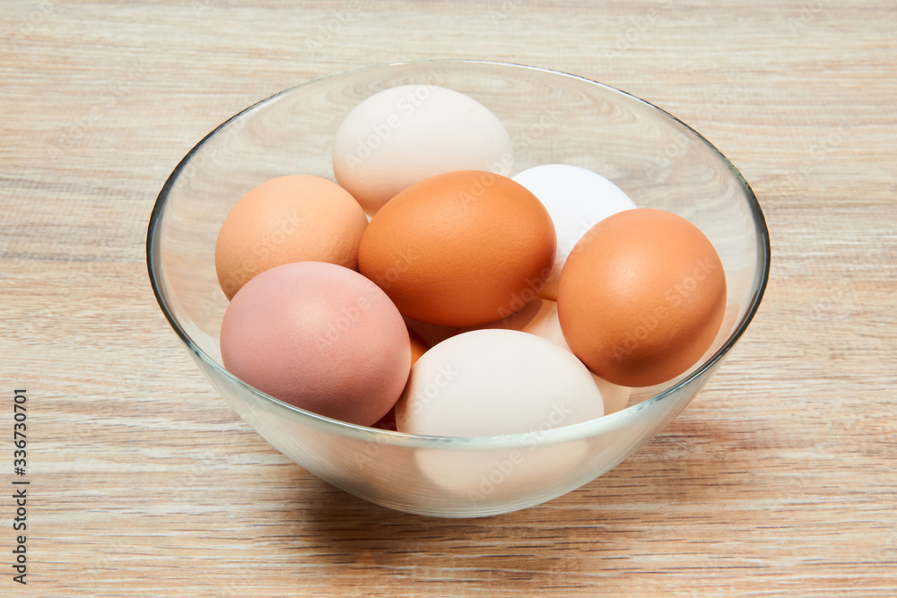 eggs of different colors in a glass bowl on a wooden table surface eggs of different colors in a glass bowl on a wooden table surface