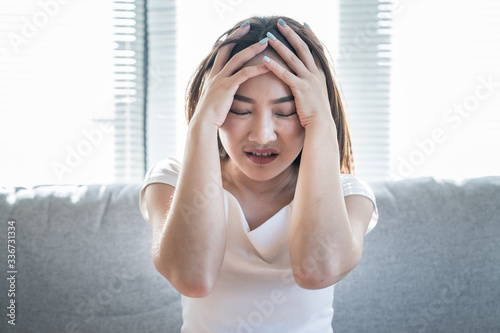 Obraz na plátne Young woman suffers from a headache while sitting on the sofa at home