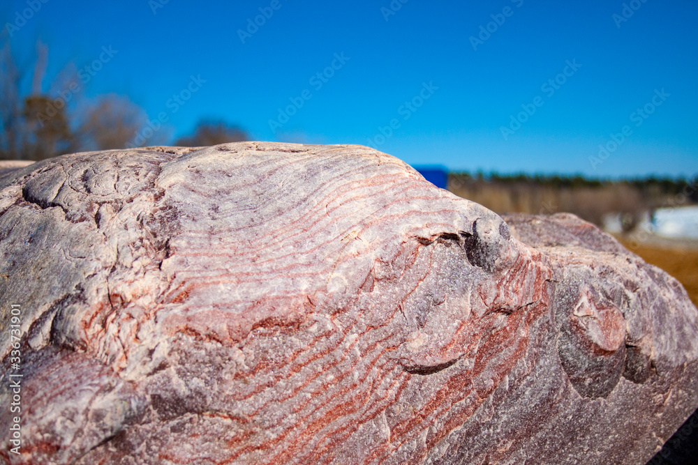 a large granite stone, with different stripes, stands on the ground, against the sky a large granite stone, with different stripes, stands on the ground, against the sky