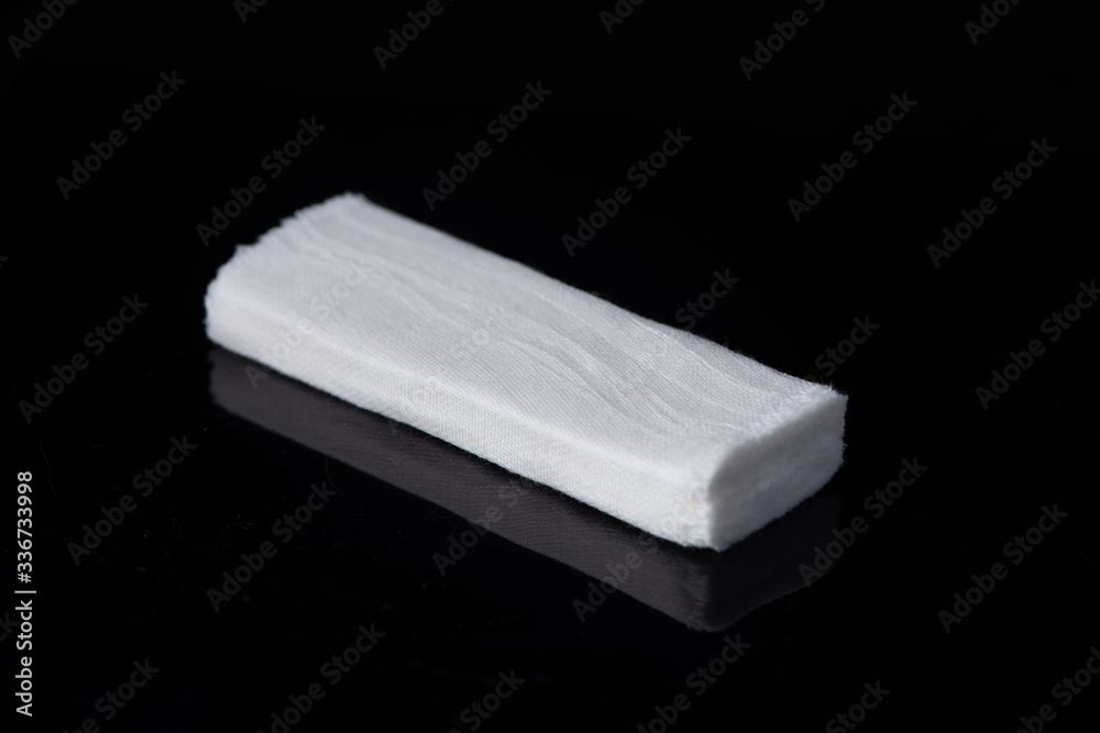 Fototapeta premium White medical cotton gauze bandage on white, black background, Medical bandage of new first aid gauze unrolling