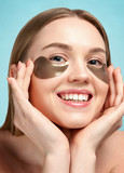 Portrait of Beauty woman with eye patches showing an effect of perfect skin. Beautiful face of young adult woman with clean fresh skin and bare shoulders on blue background. Blonde Spa Girl.
