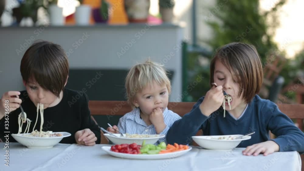 Cute children, boy brothers, eating spaghetti in garden summertime Cute children, boy brothers, eating spaghetti in garden summertime