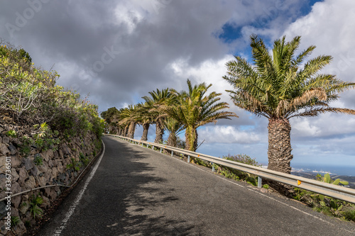 Panoramic view of asphalt road on the island coast surrounding hills around and see in a background Gran Canary island