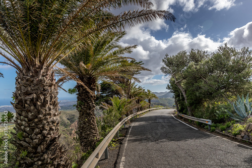 Panoramic view of asphalt road on the island coast surrounding hills around and see in a background Gran Canary island