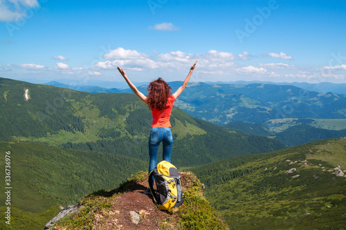 Happy young woman stands on a rock, her hands arms raised up to the blue sky