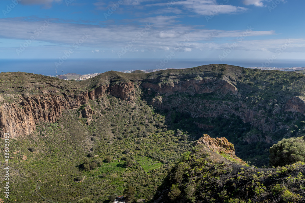 View of the hilltop on a mountainous landscape of volcanic origin along with lots of trees on the horizon, one can see the setting moon of the Gran Canary island View of the hilltop on a mountainous landscape of volcanic origin along with lots of trees on the horizon, one can see the setting moon of the Gran Canary island