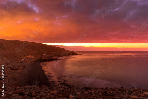 Sunrise from a cliff with moving clouds in a different direction forming a line where the sun rises on the sea and forms rays reflecting on the ocean surface from the Grand Canary.