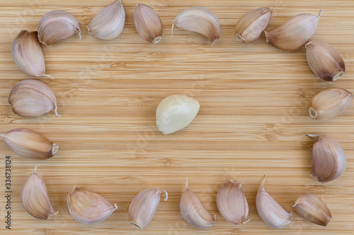 one peeled in the center and many unpeeled garlic cloves on a bamboo board