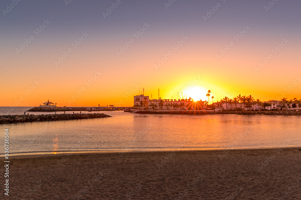 Sunset over the lagoon of orange-red clouds on the horizon and reflections of lights reflecting on sea level with urban area Grand Canary Island Valle