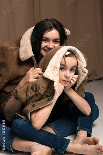 close-up portrait siblings with brown eyes in studio with brown nude texture background have a fun,laghfing, smiling, love each other in brown jackets photo