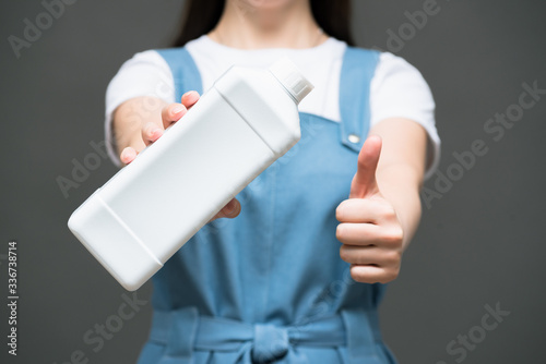 Woman with detergent bottle on gray background close up.