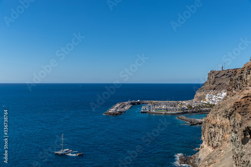 View from the air on the coast and bay in the city of Mogan on the Canary Islands where the bay harbor and people walking along the waterfront inside city © Lukas