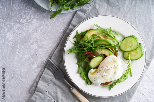 Poached eggs with herbs, avocado and cucumber served on a plate on a light background Copy space