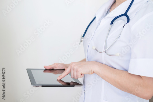 Unrecognizable female doctor in uniform uses a tablet computer. A medical worker contacts patients on a device. Cropped.