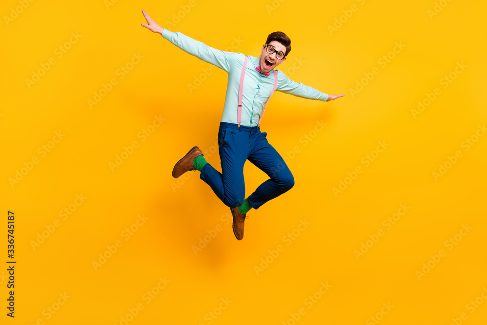 Full size photo of cool stylish guy jumping high up rejoicing good mood wear specs shirt bow tie suspenders trousers shoes green socks isolated bright yellow color background