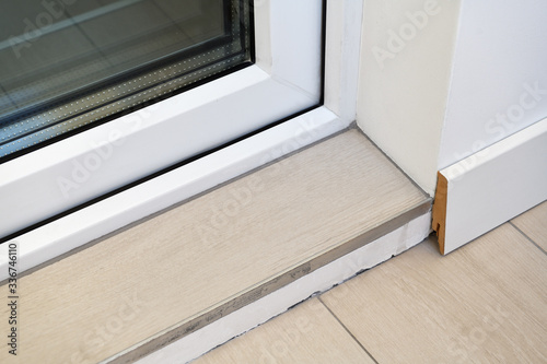 Poor decoration of the threshold of ceramic tiles. MDF skirting board is poorly installed, uneven cut. The transition between the floor and the threshold. photo