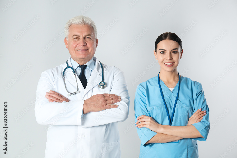 Senior doctor and young nurse against light background
