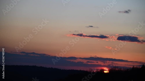 Dramatic sunset over the small clouds and forest trees. 4K time lapse with red purple orange pink dusk cloudy sky. Dramatic landscape of sky and tiny clouds. Bright orange and red sun moves down.
