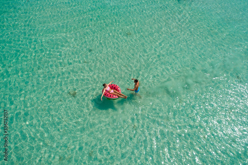 .Summer holiday fashion concept - tanning couple at the beach on a turquoise sea shot from above. Top view from drone. Aerial view of slim woman and man sunbathing lying on a beach in Thailand. © gawriloff
