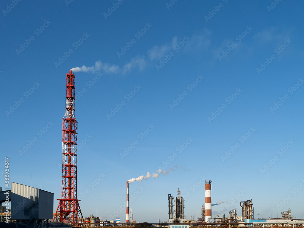 Industrial landscape. Chimneys, apparatus, equipment and communications of petrochemical plant over blue sky sunny day with copyspace. Concept of environmental pollution and nature conservation.