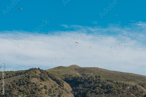 Foto Parapentes volando sobre cielo azul con nubes y sobre una montaña