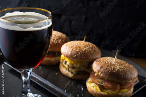 close-up, beer glasses with craft dark and light beer with foam, against a background of burgers, with a variety of ingredients, including shyomga, beef meat patty, cheese burger. In a rustic style