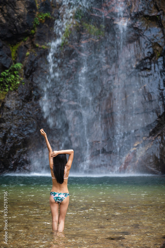 Young slim woman in Bikini enjoys rainforest waterfall in Kanchanaburi  Thailand