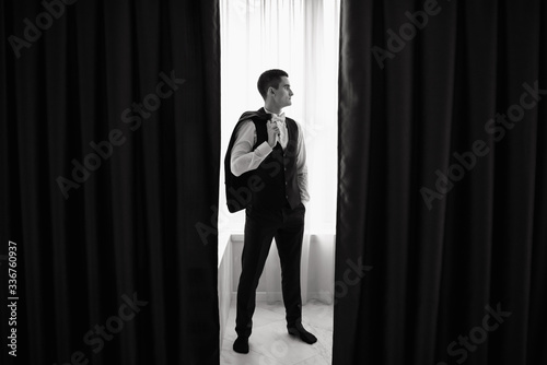 Grooms morning preparation. Preparation of groom before wedding at home. Stylish groom posing near window. Groom getting ready in the room for wed day. Copy space.