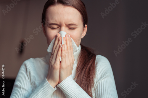 Cough in tissue covering nose and mouth when coughing. European woman sick with flu at home.