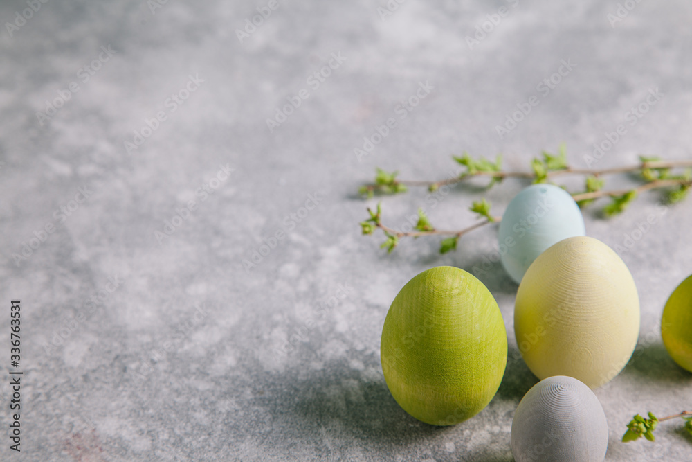 Happy easter concept. Multicolored easter painted eggs and branches with buds on a gray background.