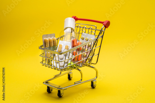 Miniature shopping trolley with medicines, antiseptic. Self-isolation. Yellow background.