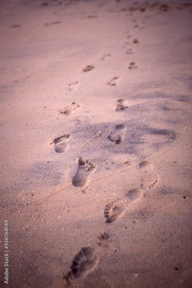 Footprints in the sand from children's feet. A girl in a pink t-shirt runs along the beach in the background. Footprints in the sand from children's feet. A girl in a pink t-shirt runs along the beach in the background.