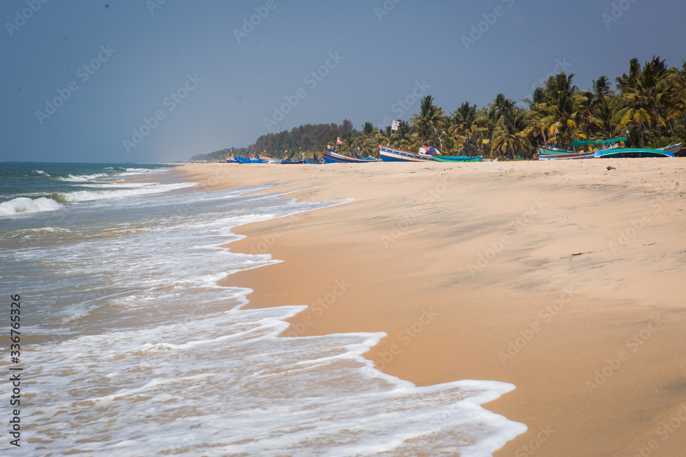 Wave with white foam on the sandy shore of the Indian ocean. The sea coast in Kerala, fishing boats in the distance on the sand, a Seagull.