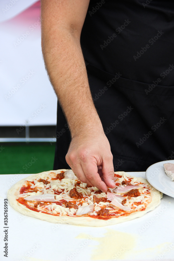 Italian cuisine. Preparation pizza with the hands of a chef. Dough, ketchup, bacon and cheese on a white board on a wooden table. Background image, copy space