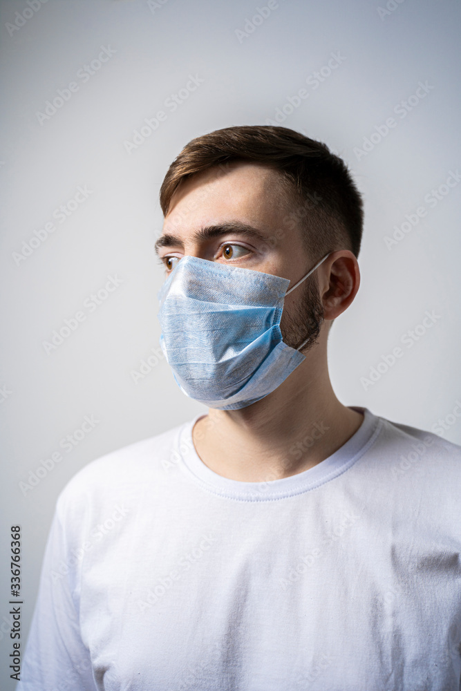 A young man in a medical mask on a white background looks away. Self isolation A young man in a medical mask on a white background looks away. Self isolation