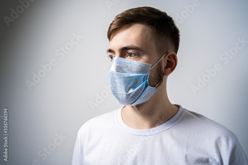 A young man in a medical mask on a white background looks away. Self isolation