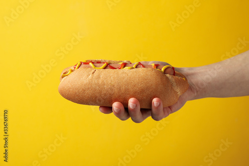 Принти на полотні Hand holds tasty hot dog on yellow background