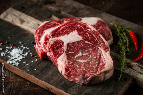 Bild auf Leinwand Fresh raw beef rib eye steak with red pepper and herbs on a wooden background