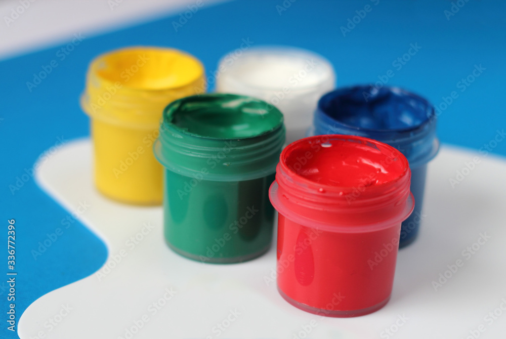 Containers of watercolor paints and white paintbrushes palette on blue background. Containers of watercolor paints and white paintbrushes palette on blue background.