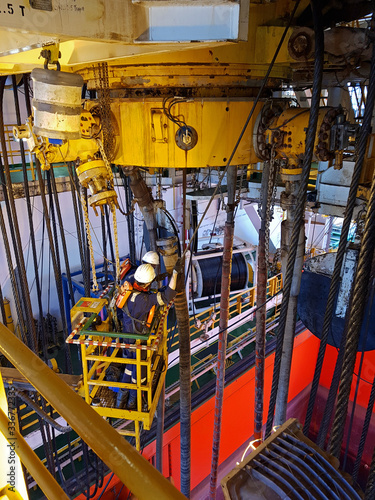 Two technicians working on a basket close to diverter of a drillship in moonpool area photo