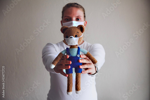 Obraz na plátně Caucasian girl in a facial mask holding a toy bear in mask in front of her