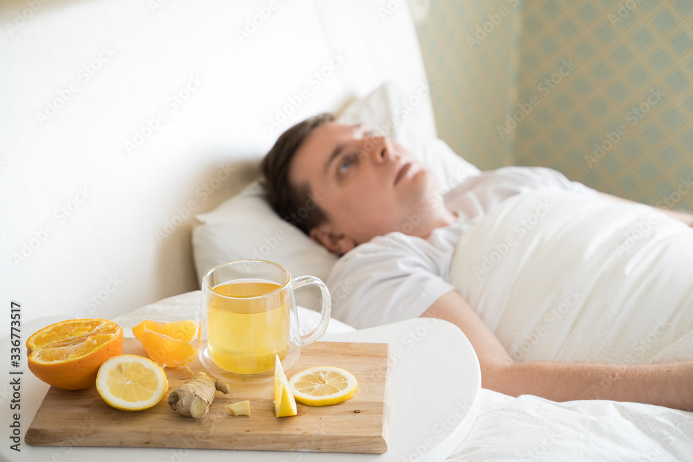 Cup with antipyretic drugs for colds,flu.Sick man in bed. Tea with citrus vitamin C,ginger root,lemon,orange.Wooden tray. Home self-treatment.Medical quarantine antiviral covid-19 coronavirus therapy Cup with antipyretic drugs for colds,flu.Sick man in bed. Tea with citrus vitamin C,ginger root,lemon,orange.Wooden tray. Home self-treatment.Medical quarantine antiviral covid-19 coronavirus therapy